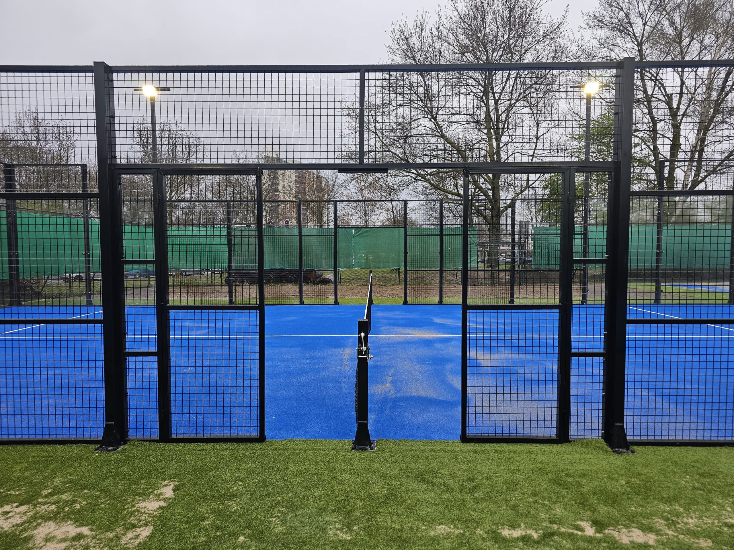 14 açık hava padel tenis kurulumu sonrası mavi zeminli çimler içerisinde bir saha