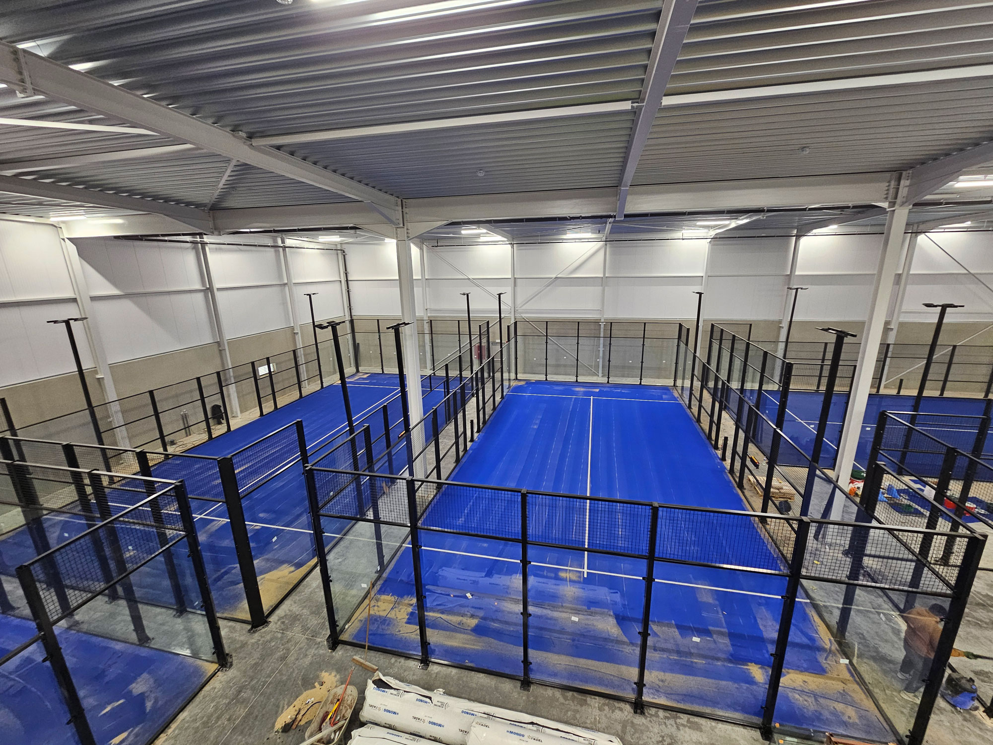 Kapalı Padel Kortu Projesi Mavi zeminli kapalı profesyonel padel kortu inşaatı ve cam paneller